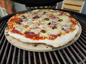 Pizza mit Salami, Oliven, Zwiebeln und mit Käse überbacken auf einem Grill